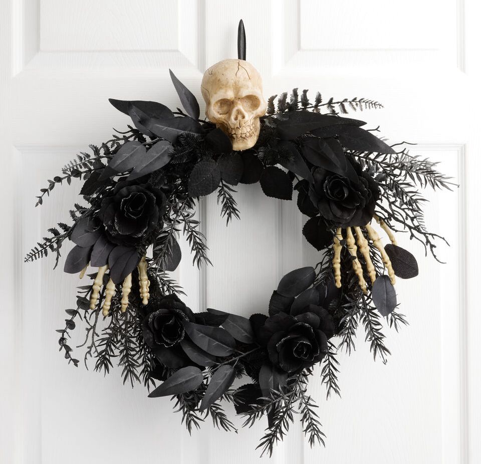 Halloween wreath with black roses, feathers, and a skull on a white door background.