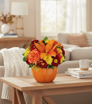 Decorative pumpkin vase with flowers on a wooden coffee table in a living room.