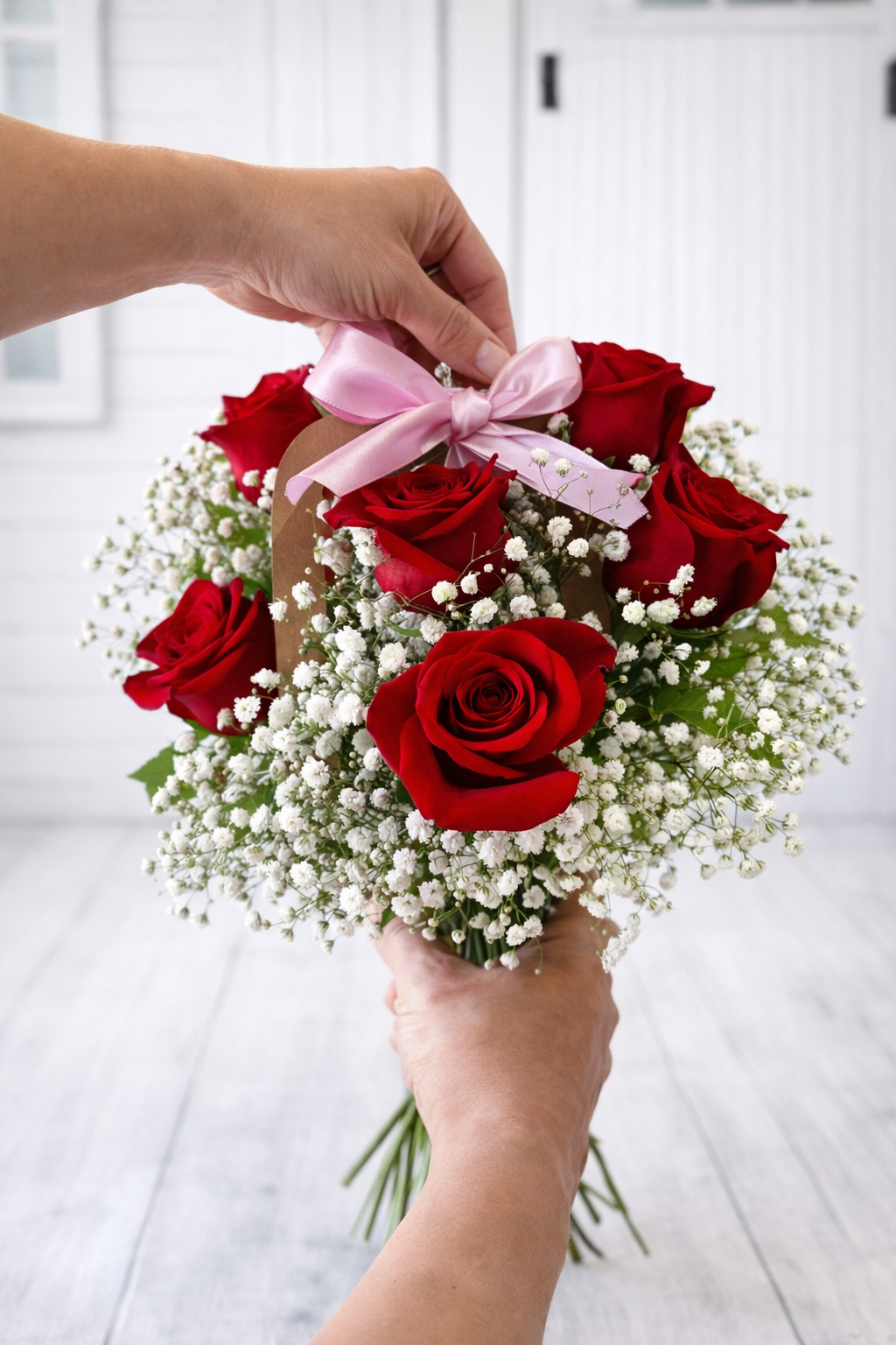 Bouquet of red roses with a pink bow held by a person against a white background