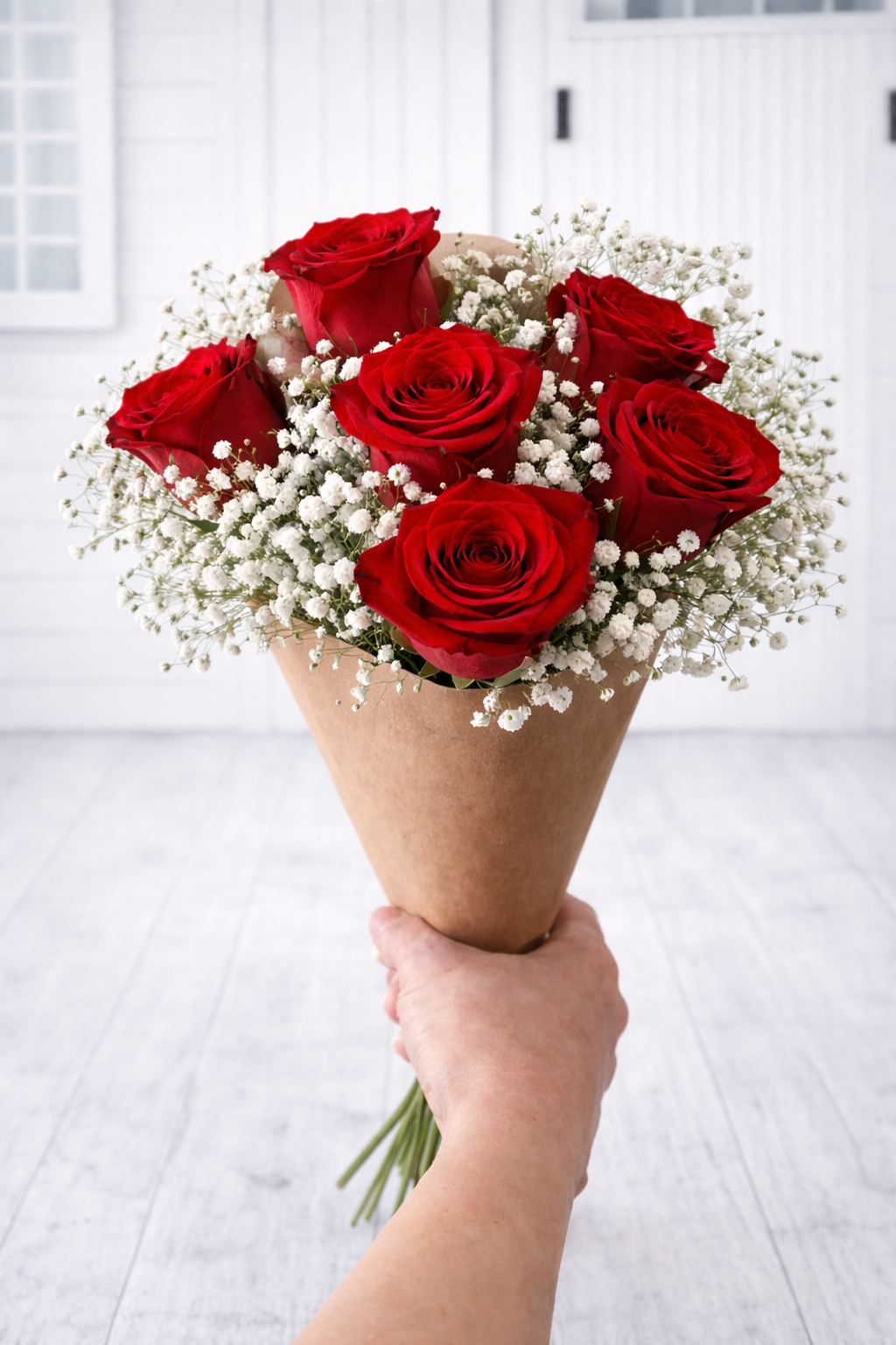 Bouquet of red roses with baby's breath held by a hand against a white background