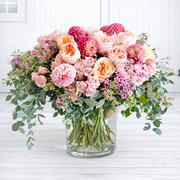 Bouquet of pink and orange flowers in a clear vase on a white wooden surface