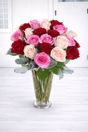 Bouquet of red, pink, and white roses in a clear vase on a white surface.