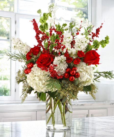 Bouquet of red, white, and green flowers in a clear vase on a table.