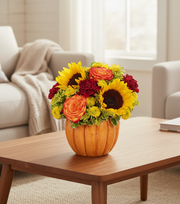 Pumpkin vase with colorful flowers on a wooden coffee table in a living room.